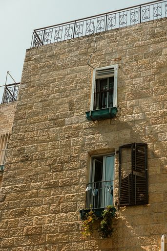 Stone building facade with open windows and a balcony under a clear sky, showcasing rustic architecture.