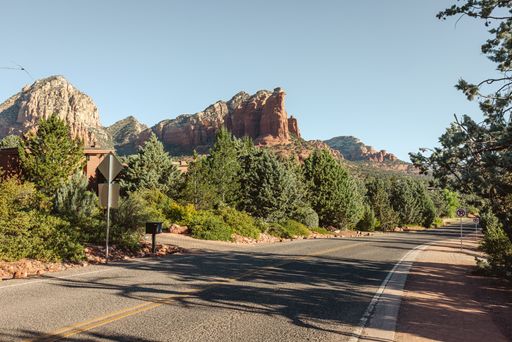 Scenic view of Sedona's red rock formations and lush greenery along a quiet road under a clear blue sky.