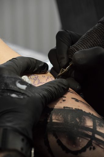 A close-up shot of an artist tattooing on someone with black gloves