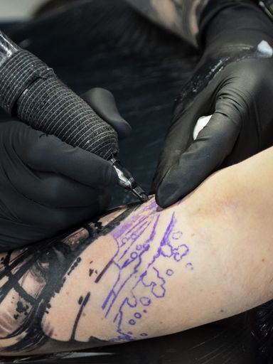 A vertical, close-up shot of a tattooist with black gloves doing a tattoo on someone's arm