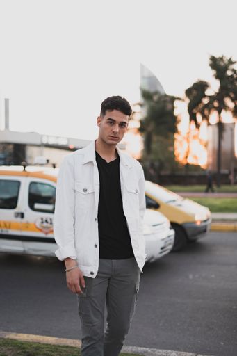 A vertical shot of a young stylish caucasian man in a white jacket posing outdoors