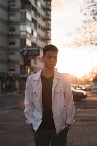 A vertical shot of a young stylish caucasian man in a white jacket posing outdoors