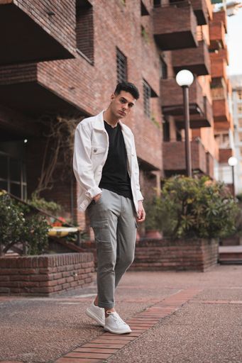 A vertical shot of a young stylish caucasian man in a white jacket posing outdoors