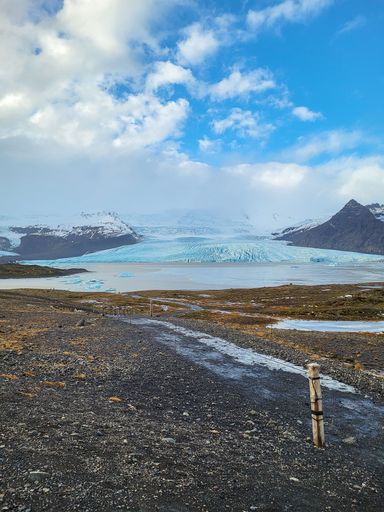 Scenic view of a glacier in Iceland under a partly cloudy sky, showcasing rugged terrain and icy waters.