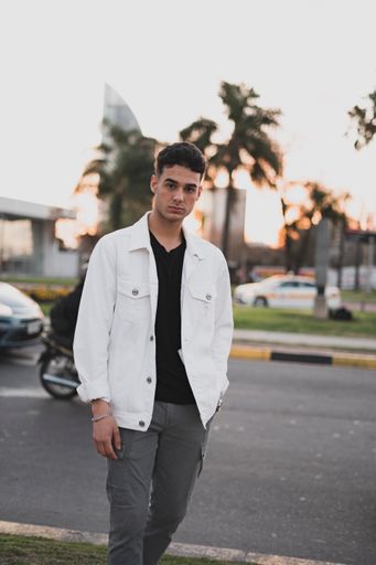 A vertical shot of a young stylish caucasian man in a white jacket posing outdoors