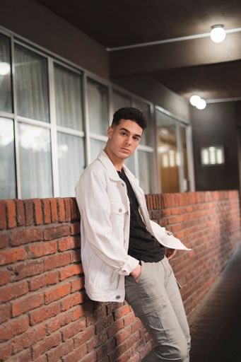 A vertical shot of a young stylish Caucasian male posing by a brick wall