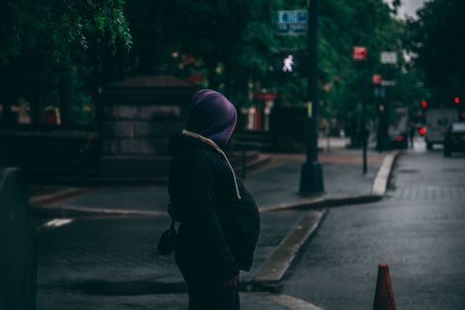 A shot of a person wearing a hoodie with hood standing at the pedestrian lane