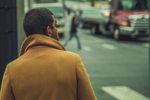 A closeup shot of a male wearing bright brown coat standing near the street with blurred background
