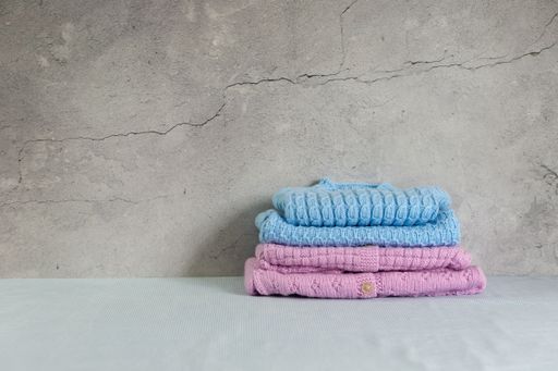 Cozy, warm blue and pink baby sweaters, knitted clothes on a table. Stack of handmade garment. Gray background with copy space and place for text.
