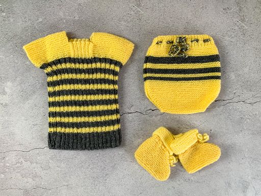 Cozy, warm yellow and black baby sweater, socks and pants. Knitted clothes on a table. Handmade garment to small children. Grey background.