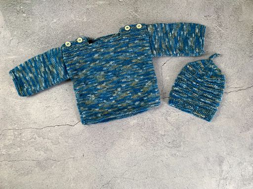 Cozy, warm blue speckled baby sweater a cap. Knitted clothes on a table. Handmade garment to small children. Grey background with copy space.
