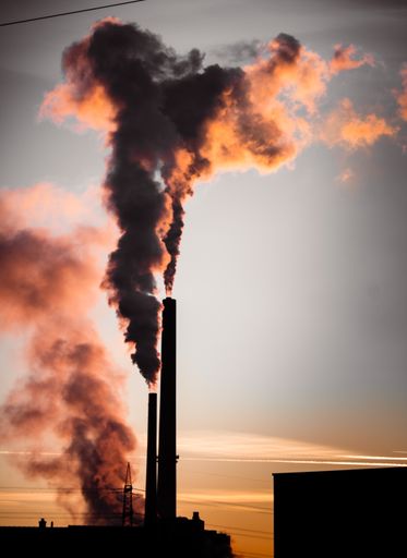 A scenic view of dark smoke coming out from pipes in an industrial plant at sunset