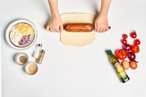 A top view of a chef making pizza with various ingredients on a white surface with a copy space