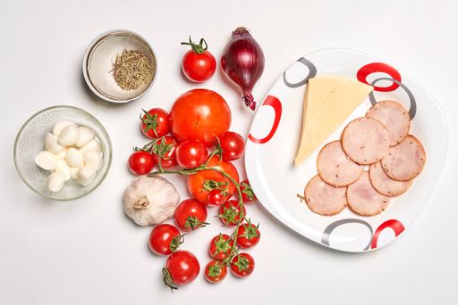 A top view of various ingredients for pizza on a white surface