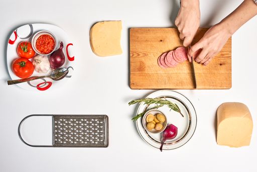 A top view of a chef making pizza with various ingredients on a white surface with a copy space