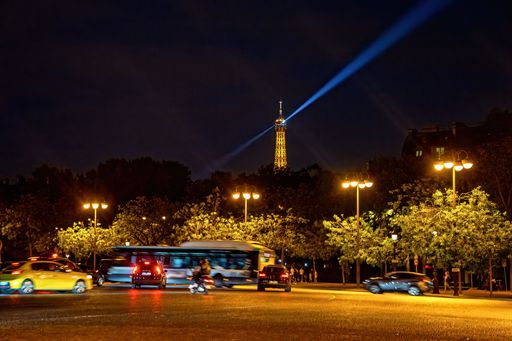 Night view of Paris with the Eiffel Tower illuminated, cars and a bus on a bustling street, capturing the vibrant city life.