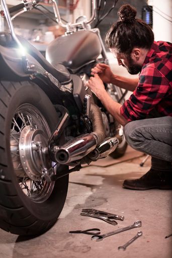A vertical shot of a German male repairing his motorcycle.