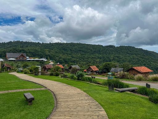 Scenic view of wooden pathway leading to rustic cabins nestled in lush green hills under a cloudy sky.