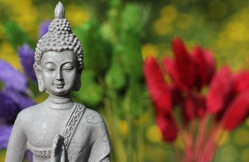 A closeup shot of the Buddha Statue in a garden with blurred flower background