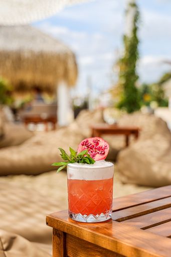 A vertical shot of an orange cocktail with mint and pomegranate slice on a wooden table during a summer vacation