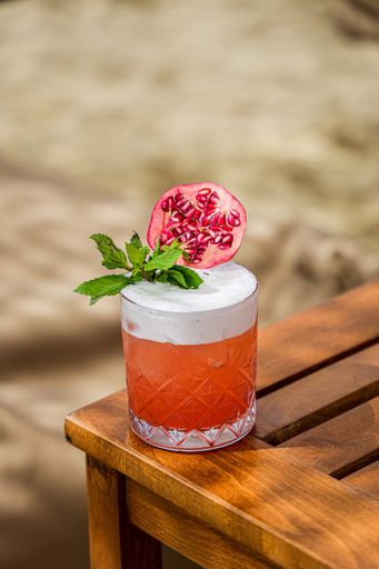 A vertical shot of an orange cocktail with mint and pomegranate slice on a wooden table during a summer vacation