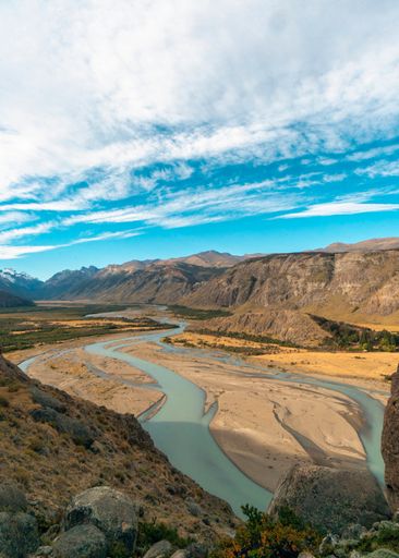 A beautiful view of the flowing Las Vueltas river surrounded by mountains under the cloudy blue sky