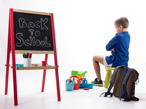 A back to school background - a little boy sitting on a chair with his arms crossed