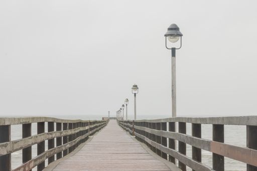 A wooden bridge over the seawater with outdoor lamps on a foggy day
