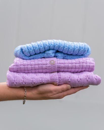 Female hand holding stacked folded baby clothes. Cozy knitted sweaters. Handmade garment to small children. A gift to needy,  donation concept.