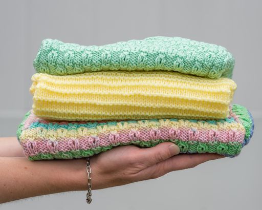 Female hand holding stacked folded baby clothes. Cozy knitted colorful sweaters. Handmade garment to small children. A gift to needy people.