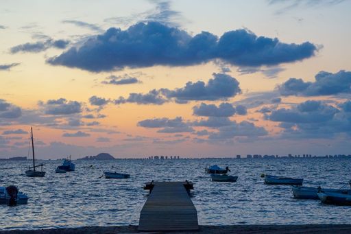 Scenic sunset view over the ocean with boats and a wooden pier, under a sky filled with clouds, capturing a serene coastal atmosphere.