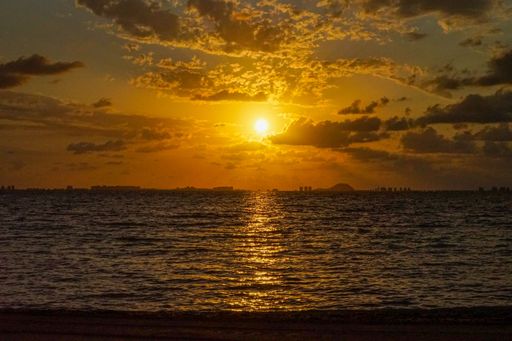 A stunning sunset over the ocean with vibrant orange hues and silhouetted city skyline in the distance.
