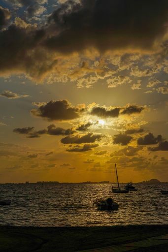 A stunning sunset over a calm sea with silhouetted boats and dramatic clouds, creating a peaceful and picturesque scene.