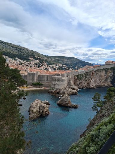 Scenic view of Dubrovnik's historic city walls and clear turquoise waters under a partly cloudy sky.