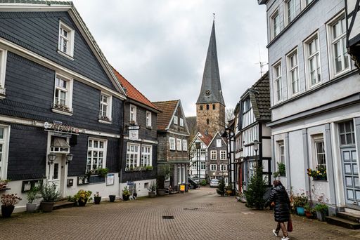 Charming European village street with traditional half-timbered houses and a church steeple, featuring a person walking on a cloudy day.