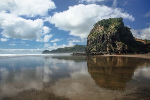 Scenic view of Piha Beach, New Zealand, with Lion Rock and clear reflections under a bright blue sky.