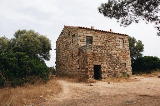 An old abandoned stone building surrounded by greenery under a cloudy sky
