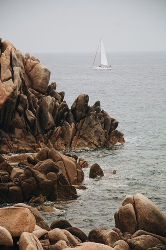 A vertical shot of a rocky shore surrounded by the sea under a cloudy sky
