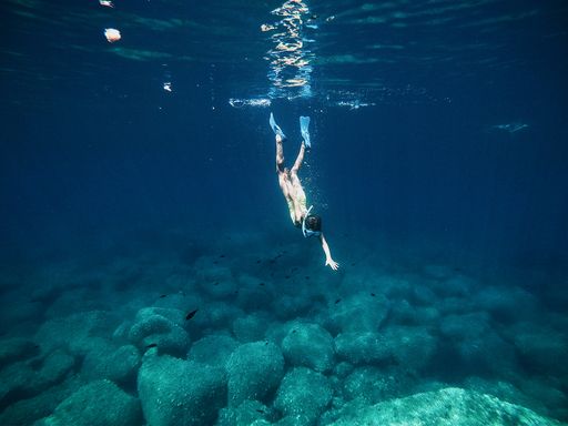 An adult person diving in the sea under the sunlight through the water waves