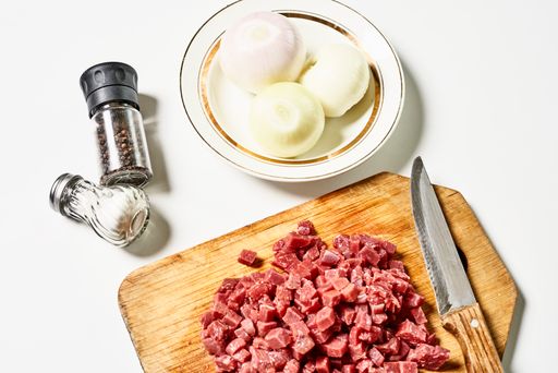 A closeup of freshly chopped meat with onions and seasonings on a white surface