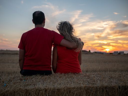 A back view of a romantic young couple in matching shirts looking at the sunset on a beach