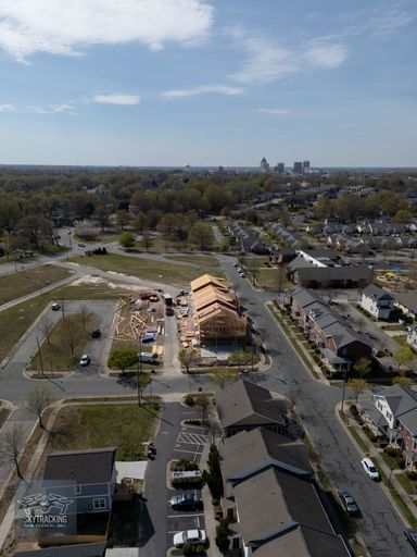 Aerial view of urban residential construction site with city skyline in the background under a partly cloudy sky.