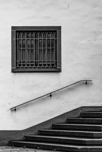 A vertical grayscale shot of the outside of a building with stairs and a window