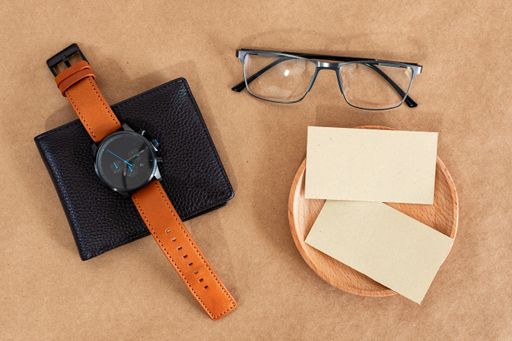 A top view of gentlemen's accessories on the wooden background. Watch, money pockets, eyeglasses, business cards on rustic brown background