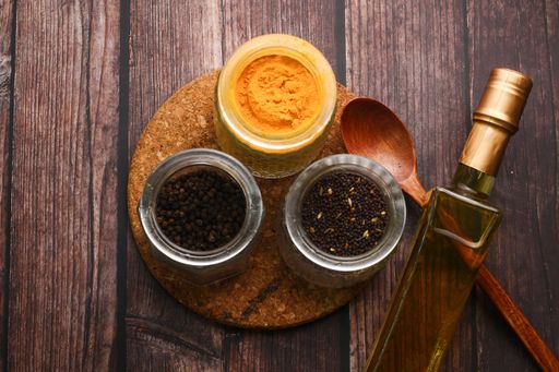 A top view of various seasonings, a bottle of oil, a chopping board, and a wooden spoon on a table