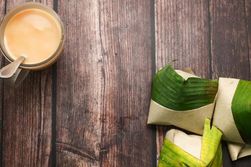 A top view of coconut flavored rice wrapped in banana leaves and a drink on a table