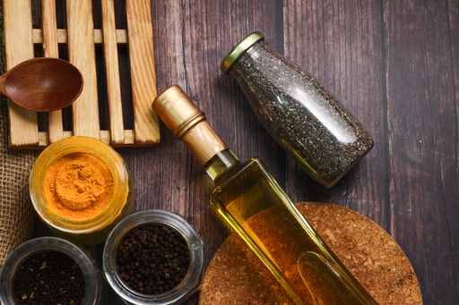 A top view of a bottle of oil, various seasonings, chopping boards and a wooden spoon a table
