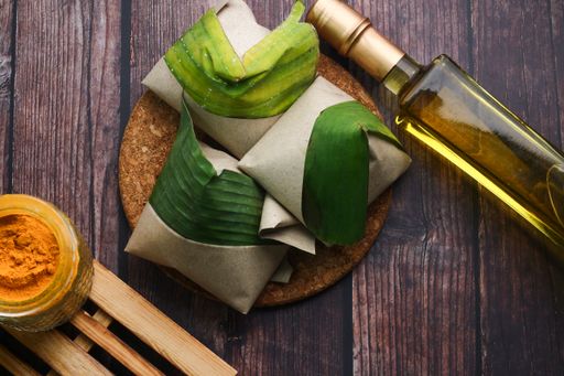 A top view of coconut flavored rice wrapped in banana leaves and a bottle of oil on a table