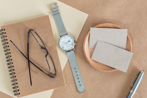 Flat lay of watches, accessories, and business cards on modern rustic brown paper at a home office desk