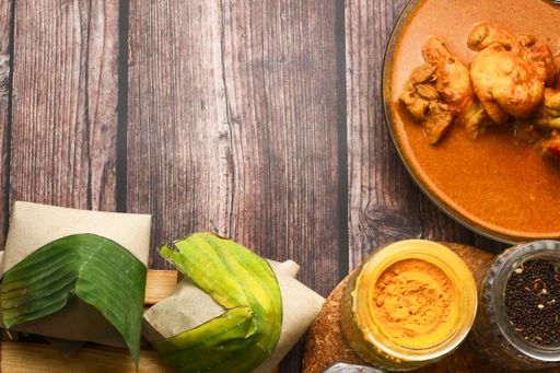 A top view of coconut flavored rice wrapped in banana leaves and various seasonings on a table